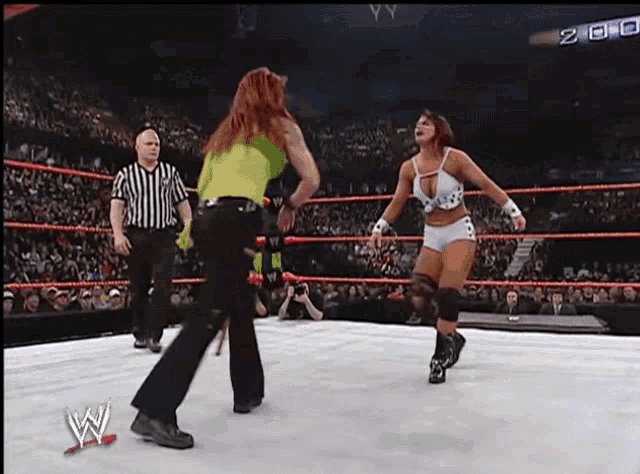 two women wrestling in a wrestling ring with a referee and a sign that says w on it