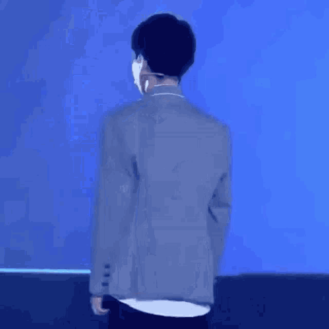 a man in a gray jacket is standing in front of a blue wall .