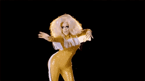 a drag queen is wearing a yellow jumpsuit with fringe and a feathered wing .