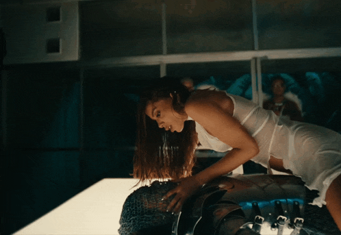 a woman in a white tank top is kneeling on a person 's back