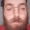 a man with a beard and glasses is wearing a red shirt and making a funny face .