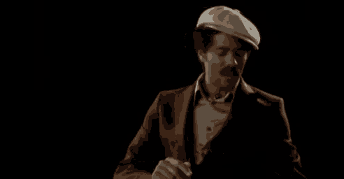 a man wearing a hat and a suit is holding something in his hands in a dark room .