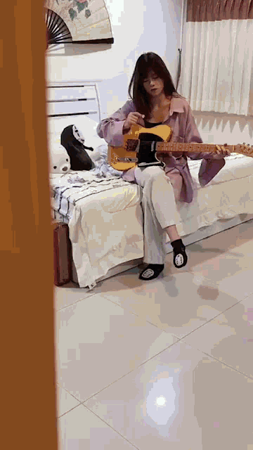 a young woman is sitting on a bed playing a guitar .