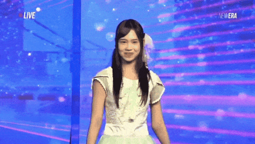 a woman in a white dress stands in front of a blue screen that says live on it