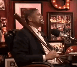 a man in a suit and tie is holding a baseball bat in front of a microphone