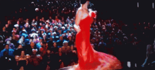 a woman in a red dress is walking down the runway in front of a crowd .