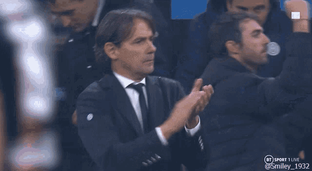 a man in a suit and tie applauds in front of a bt sport live logo