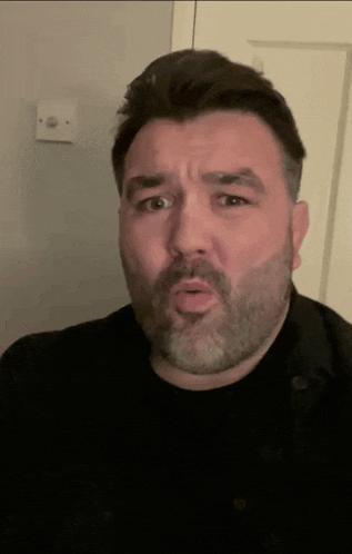 a man with a beard is making a funny face in front of a door