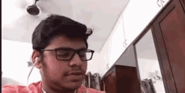 a man wearing glasses and headphones is sitting in a room with a fan on the ceiling .