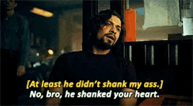a man with a beard is talking to another man in a dark room while sitting at a table .