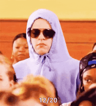 a man wearing a hoodie and sunglasses is standing in a crowd of people .
