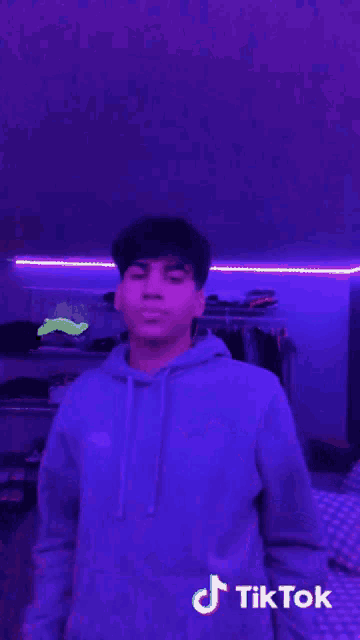 a young man wearing a purple hoodie is standing in front of a purple wall .