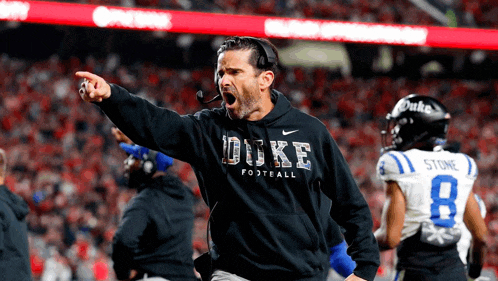 a man wearing a duke football sweatshirt shouts on a football field
