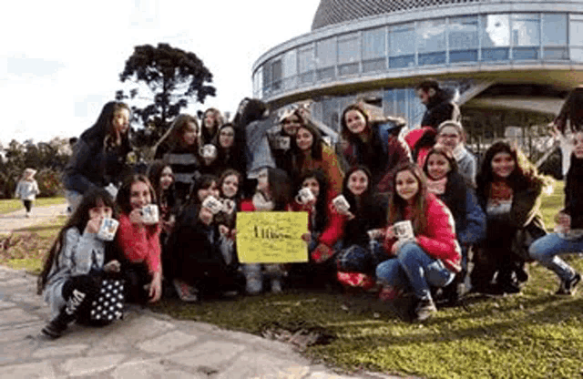 a group of young girls are posing for a picture in front of a building holding cups .