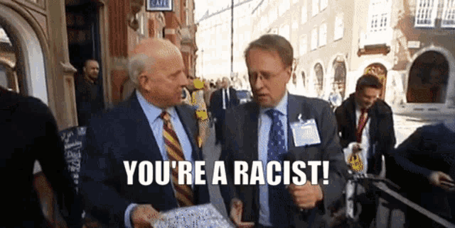 a man in a suit and tie says you 're a racist while talking to another man