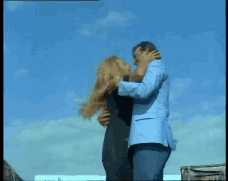 a man and a woman are hugging each other in front of a blue sky
