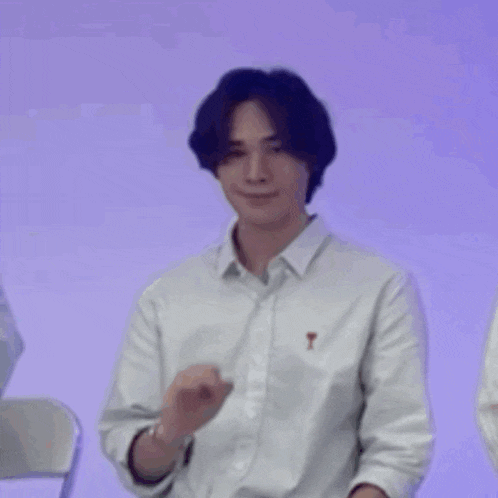 a young man in a white shirt is sitting in a chair and making a funny face .