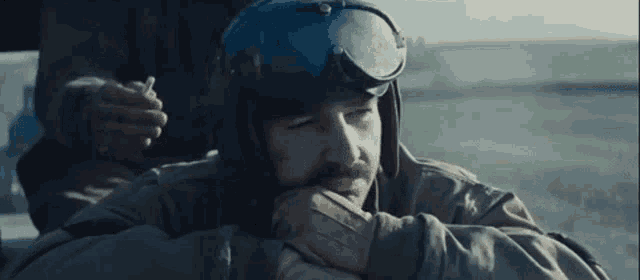 a man with a beard is wearing a helmet and goggles while smoking a cigarette .