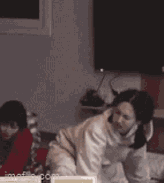 a woman in a white hoodie is sitting on a bed in a room .
