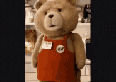 a teddy bear wearing a red apron and a help badge is standing in a kitchen .