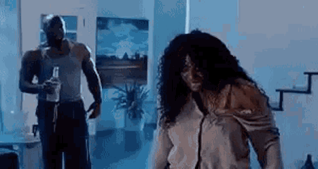 a man and a woman are dancing in a living room while the man is holding a bottle of alcohol .