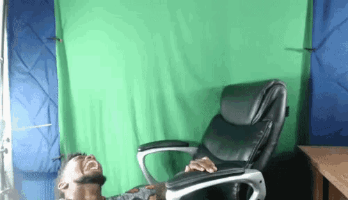 a man is sitting in a chair in front of a green screen