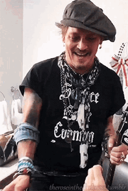 a man wearing a black shirt that says " silence evening " is holding a guitar