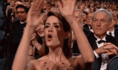 a woman in a dress is raising her arms in the air while sitting in a crowd .