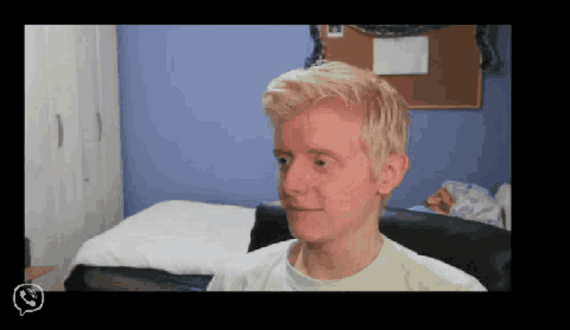 a man with blonde hair is smiling in front of a bed