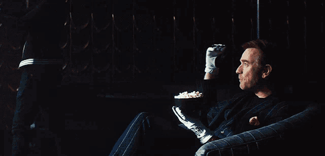 a man is sitting in a chair with a bowl of popcorn in his hand