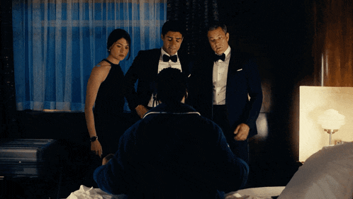 a man in a tuxedo and a woman in a black dress stand around a man in a robe