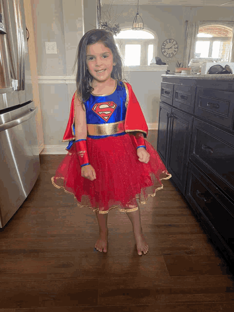 a little girl in a supergirl costume stands in front of a clock
