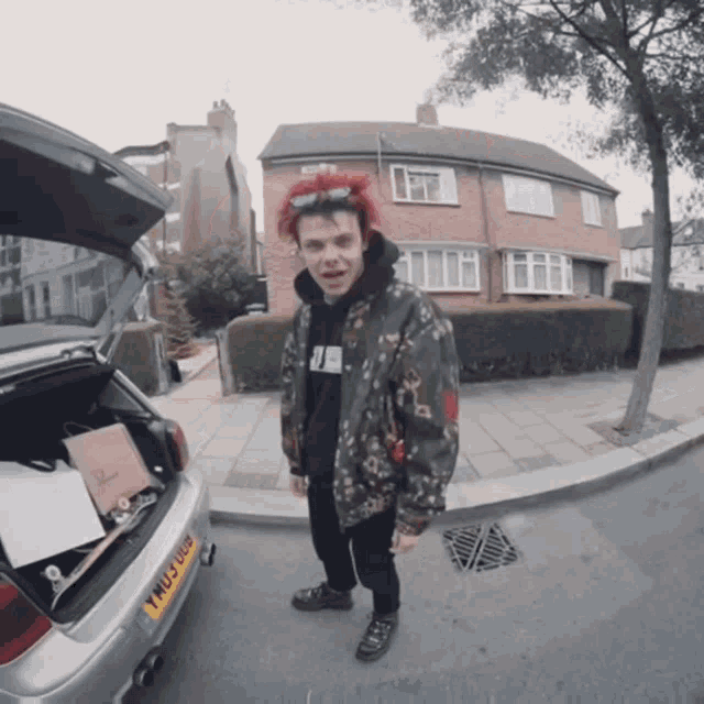 a man with red hair is standing in front of a car with a license plate that says yhu 068