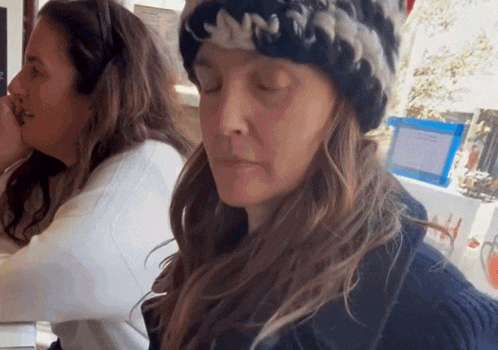 a woman wearing a knitted hat is sitting next to another woman with her eyes closed