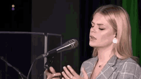 a woman is singing into a microphone while wearing a plaid jacket and earrings .