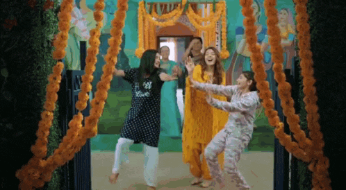 a group of women are dancing in front of a doorway decorated with marigolds .