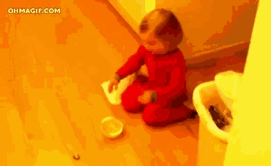 a baby in a red pajama is sitting on the floor playing with a bowl .