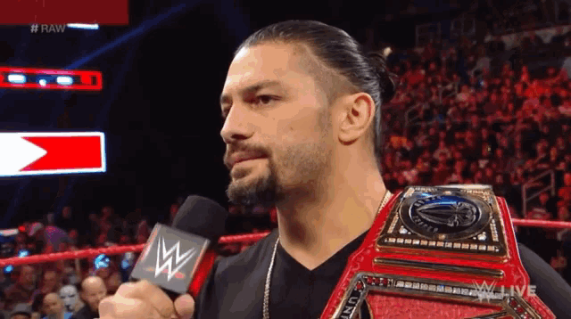 roman reigns is holding a microphone while wearing a wrestling belt