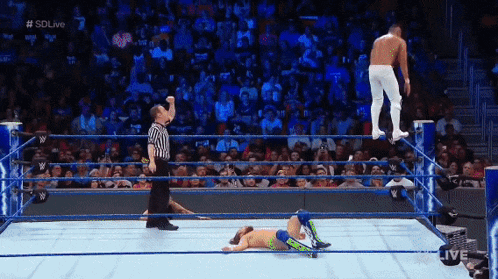 a wrestler is laying on the ground in a wrestling ring while a referee watches
