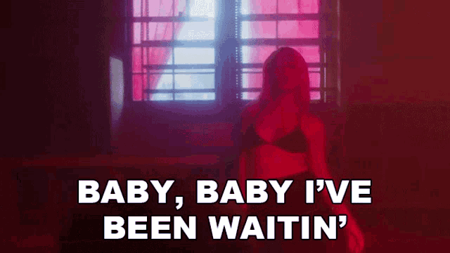 a woman in a black bra is standing in front of a window and says " baby baby i 've been waitin "