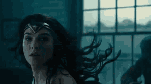 wonder woman is standing in front of a window in a dark room .