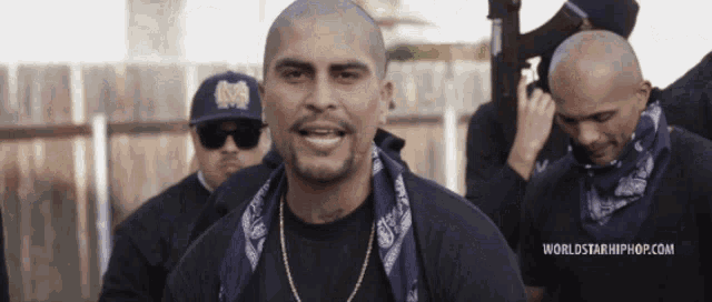 a man with a bandana around his neck is standing in front of a worldstarhiphop.com banner