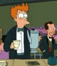 a man in a tuxedo is standing at a table holding a cup of coffee and a blender .
