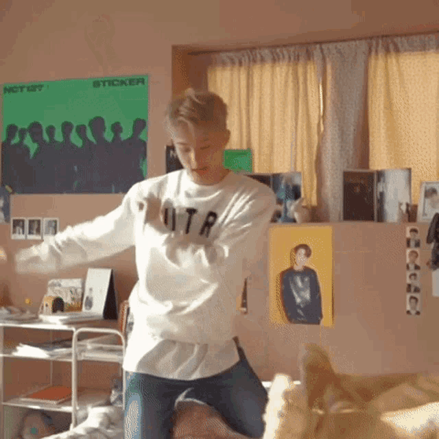 a young man is dancing in a bedroom with a poster on the wall that says sticker .