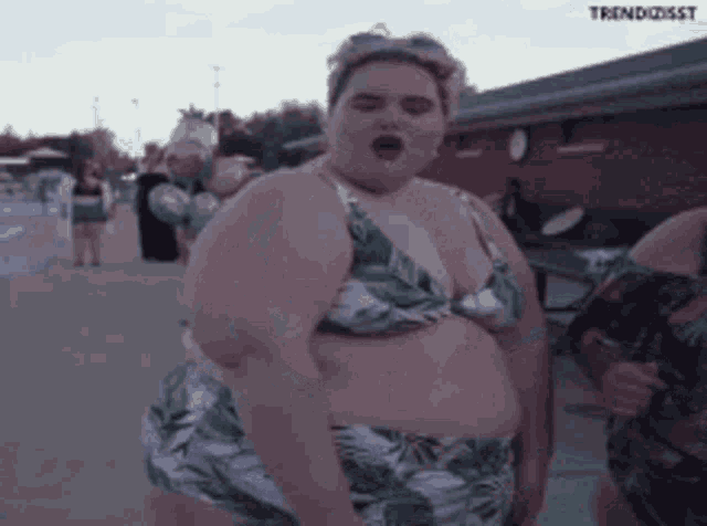 a very fat woman in a bikini is standing on the sidewalk .