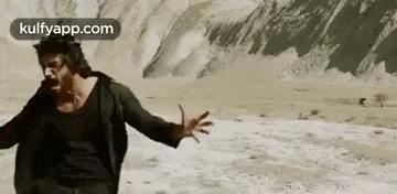 a man is running in the desert with his arms outstretched and mountains in the background .