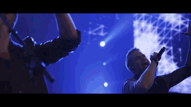 a man singing into a microphone while another man stands behind him