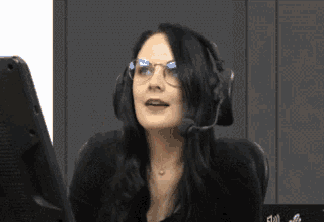 a woman wearing glasses and a headset is sitting in front of a computer monitor