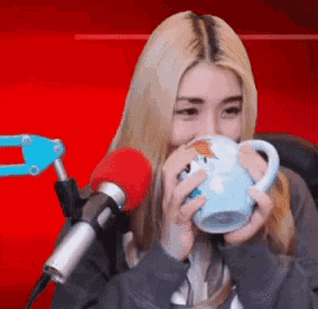 a blonde woman is drinking from a blue mug in front of a red background .