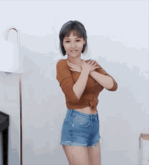 a woman in a brown crop top and blue shorts is dancing in a room .